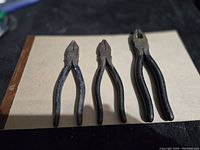 Three pairs of needle nose pliers with black handles vary in size, showing signs of wear and rust.