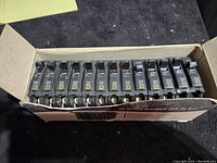 Box containing 12 black 13-20 amp circuit breakers aligned in a row.