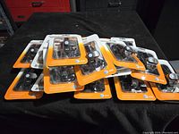 Eighteen AT&T car phone chargers in their original packaging arranged on a black surface, showing the front packaging design with clear plastic and orange/white cardboard backing.