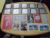 Photo showing 19 baseball cards from various players including Mickey Mantle, Babe Ruth, Mel Ott, Cal Ripken, Tim Raines and a Steeler series card among others laid flat on a wooden table.