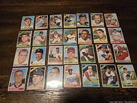 Photo showing 28 vintage 1966 Topps baseball cards featuring various players in color images, arranged on a wooden surface.