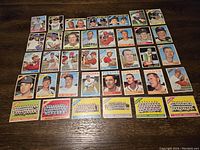 Thirty-seven baseball cards laid out on wooden surface showing mix of player portraits and team photos from mid-1960s Topps sets.