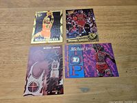 Photo showing 4 Michael Jordan basketball cards laid out on a wooden surface, each with different images and styles.