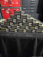 Pile of boxed OtterBox phone cases stacked on a table against red and black drawers, boxes sealed and tagged with labeling including model number.