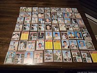 Top-down photo of 56 1970 Topps baseball cards laid on a wooden surface, arranged in rows including rookies, star players, and team checklists.