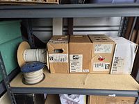 Six spools of ADT branded wires on industrial shelving, with two spools unboxed and four spools boxed.