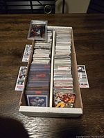 Full view of box containing two rows of vintage football cards, some in protective sleeves, and many loose cards stacked.