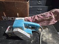 Photo of the Makita belt sander showing the whole tool with the red dust collection bag attached.