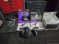 Photo showing two boxed On-Stage desk microphone stands, Knoxgear shockmount, Sony camera bag, and microphone accessories on table surface.