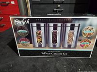 Front view of the boxed 3-piece canister set showing the stainless steel finish and window design plus sample contents.