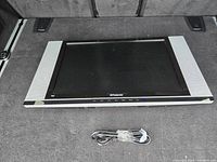 Front view of the Polaroid wall mounted TV with grey side panels, Polaroid logo on front, screen visible, and original power cable placed in front.