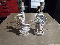 Front view of the two ceramic figurine lamps showing the man and woman, lamp sockets, and attached cords.