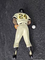 Back view of the ceramic Willie Mays figurine showing number 24 on uniform and helmet, positioned on a black fabric with a golf ball for scale.