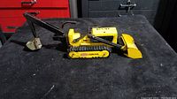 Side view of the vintage Tonka Trencher Bulldozer showing yellow and black metal construction, movable arm, and tracks with Tonka Trencher logo.