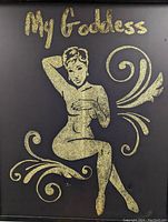 Close up photo of the gold glittery stylized female figure and the title 'My Goddess' on black board.