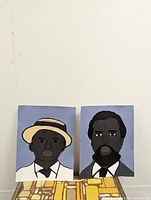 Two original draft paintings shown side by side against a wall, with one depicting a man in a beige hat and the other a bearded man in a suit.