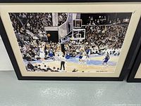 Close-up photo of one vintage basketball print by Brad Bennett in a black frame with white mat, showing a detailed basketball game scene with players and referee.