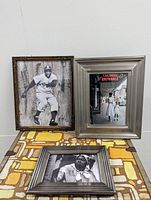 Lot of three framed artworks on white wall: vintage style baseball player mixed media collage in wood frame, colored print by Gordan Parks in silver frame, and black and white Hattie McDaniel print in dark frame