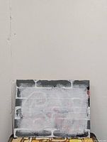 Front side of original graffiti painting showing black and white brick background with white and red spray paint obscuring original design.