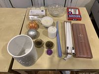 Overview of entire candle lot on table showing packaged taper candles, ceramic holder, pillar candle, spherical decorative candles, tea light holders, and glass bowl