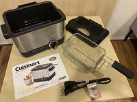 Cuisinart compact deep fryer with removable lid, basket with detachable handle, power cord, and instruction booklet arranged on a flat surface.