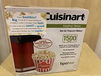 Box front showing brand Cuisinart, EasyPop series, features like 1500 watts, BPA free, large chute design, makes 15 cups in under 3 minutes, no oil required, removable butter warming/measuring cup, easy on/off control.