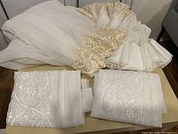 Curtains folded and placed on a table showing white sheer fabric with gold embroidered floral patterns.