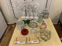 Top-down photo of decorative lot items on a table including angel statue, clock, ceramic figurines, candle holder, glass dish, and bamboo boards.