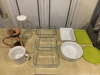 Photo showing French press, glass jug with lid, white porcelain cup, round white porcelain dish, three clear rectangular glass baking dishes, and two plastic food storage containers with green lids.