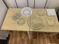 Top view of entire lot showing glass butter dish, multiple clear glass plates and bowls, square white plate, and floral patterned ceramic plate.