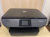 Front view of a black HP ENVY 5640 e-All-in-One printer with power button, touchscreen display, and input/output trays.
