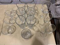 Photo showing 6 tall cylindrical clear drinking glasses, 3 short rounded glasses, and 3 stemmed wine glasses on table