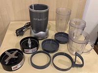 NutriBullet motor base, three plastic blending cups, two blade assemblies, and sealing rings on table.