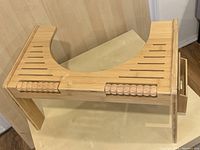 Wooden footstool with curved cutout to fit around toilet base, showing carved details and slotted top surface