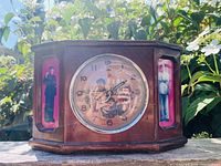Front view of the wooden mantel clock showing the circular clock face with revolutionary images and side images of Chairman Mao.