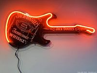 Front view of illuminated Jack Daniel's guitar neon sign on white wall.