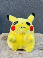 Front view of yellow Pikachu plush with red cheeks and black-tipped ears on wooden surface.