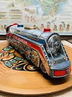 Front-left angled view of the Silver Mountain tin toy train on wooden surface with map backdrop.