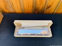 Top-down view of harmonica inside white plastic case showing Suzuki branding engraved on the metal harmonica surface.