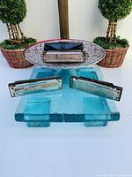 Three metal and wood Marine Band harmonicas displayed on glass and ceramic stands, two without cases and one with a black plastic case.