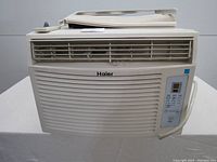 Front view of Haier window air conditioner showing vent, control panel, and remote control on top