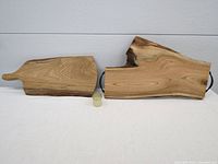 Both butternut wood boards side by side with jar of finish in front. One is a charcuterie board with a narrow handle and smooth edges. The other is a serving board with black metal handles and a natural live edge.