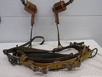 Full view of climbing belt with attached spurs showing leather and yellow fabric materials, metal buckles, and straps.