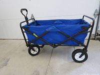 Side angle showing blue fabric wagon with black metal frame, wheels, and handle with some rust visible on frame.