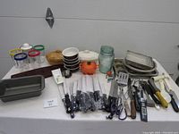 Overview of assorted kitchen items on table showing baking pans, dishes, glasses, utensils, and knives