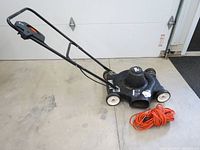 Side view of the Black & Decker electric lawnmower with handle/lever and coiled orange extension cord on concrete floor.