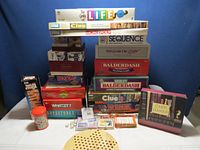 Stack of boxed board games including The Game of Life, Monopoly, Sequence, Win Lose or Draw, Balderdash, Absolute Balderdash, Clue, Risk, and card games with jenga and boggle included.