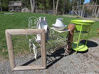 Full view of lot outdoor with all items: garden bench, birdhouse, enamel jug and bowl, wooden frame, carved wooden ornament, and lime green metal ice bucket stand.