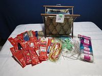 Wide shot of knitting needles in red packaging, plastic cable needles, measuring tape, yarn skeins, and knitting basket