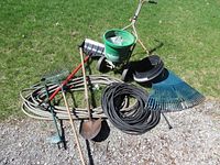 Full view of lawn and garden tools including Lawncrafter fertilizer spreader, hoses, rakes, shovels, and weed puller.